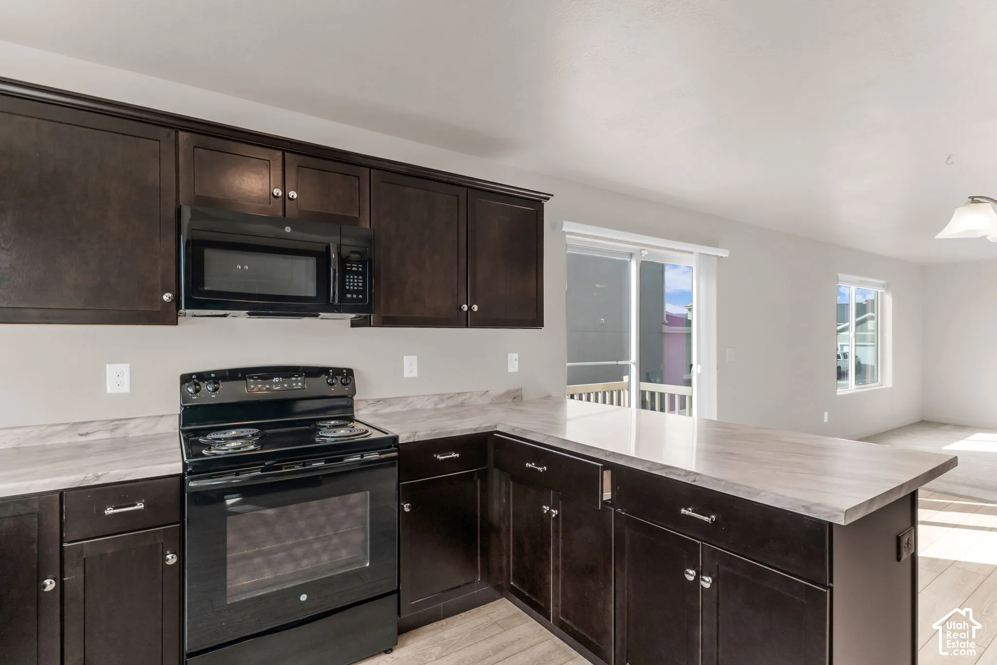 Kitchen featuring dark wood-finish cabinetry, black appliances, light-toned countertops, and wood-finish flooring
