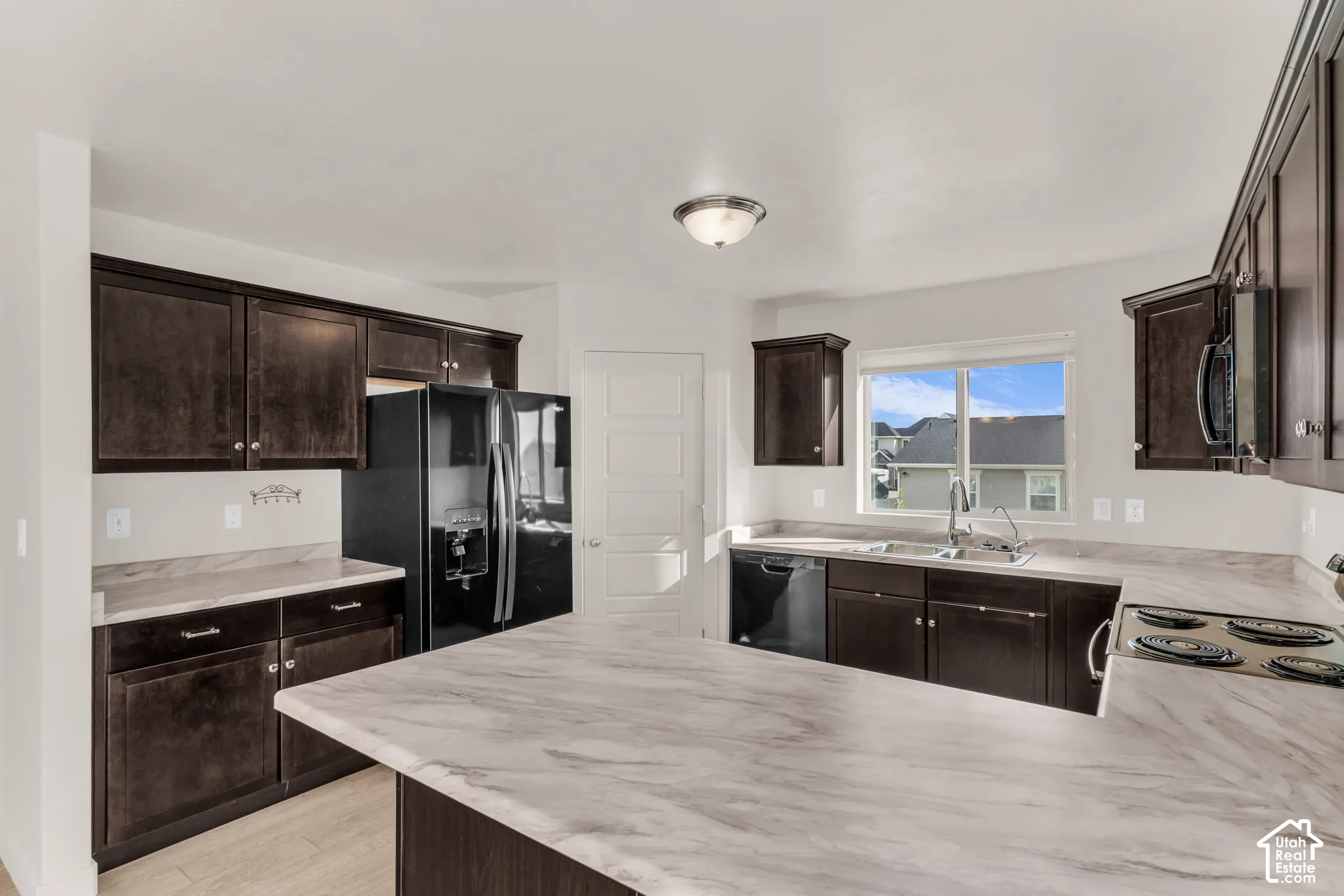 Kitchen featuring dark wood-finish cabinetry, light-toned countertops, and a stainless steel sink