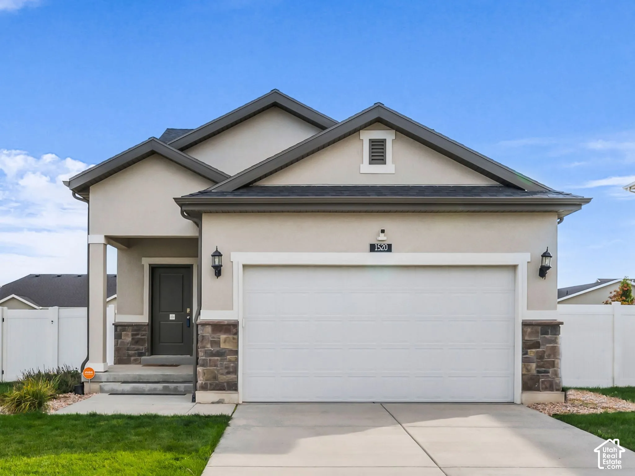Stucco exterior with stone accents, dark asphalt shingle roofing, attached two-car garage, and a front entry door with side lighting fixtures