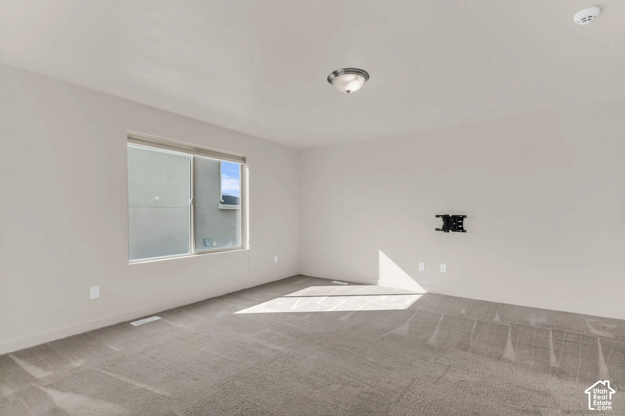 Wall-to-wall carpeting, single window, flush-mount ceiling light fixture, wall-mounted television bracket