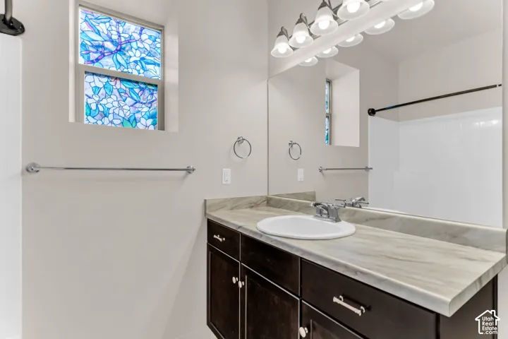 Built-in vanity with a single sink, chrome faucet, wood-finish cabinetry, and a large wall-mounted mirror with overhead lighting