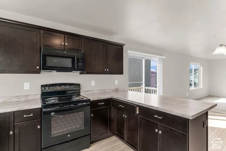 Kitchen featuring dark wood-finish cabinetry, black appliances, light-toned countertops, and wood-finish flooring