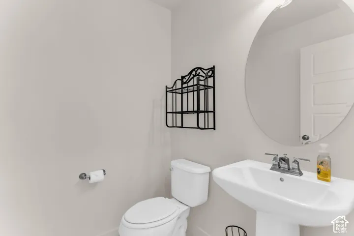Pedestal sink with chrome faucet, circular wall mirror, and a white toilet