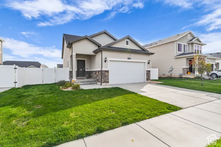 Stucco exterior with stone accent, concrete driveway, attached garage, and a white privacy fence