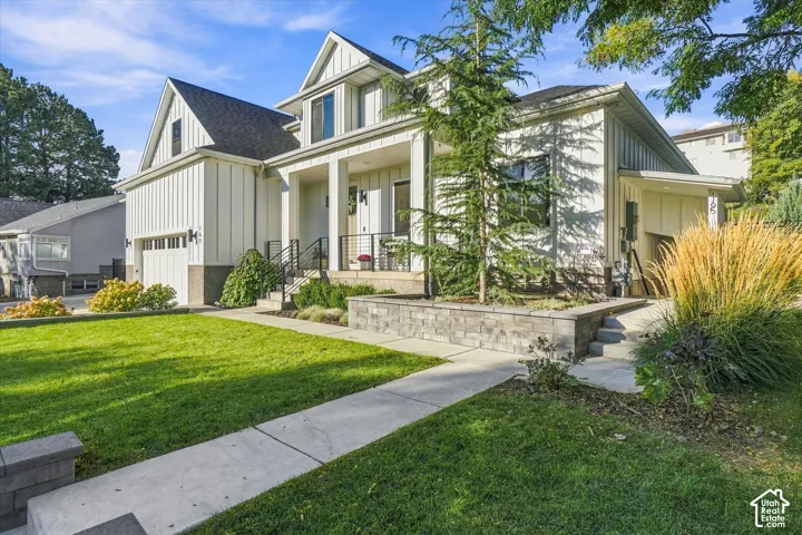Modern farmhouse exterior with vertical board and batten siding, a covered front porch, an attached garage, and a tiered stone retaining wall