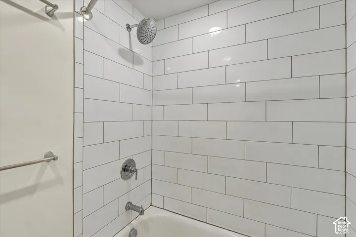 Tub and shower combination featuring white subway tile, a rain showerhead, and a towel bar