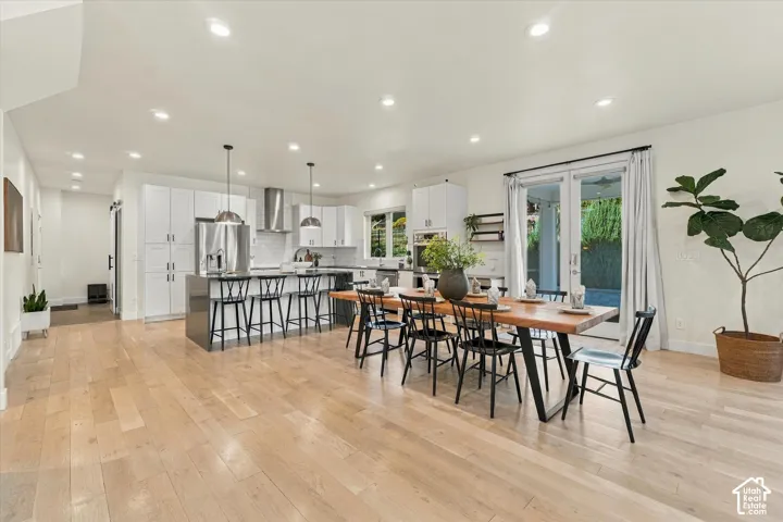 Expansive living area with light wood-finish flooring, white cabinetry, a large kitchen island, stainless steel appliances, and double glass doors leading to the exterior
