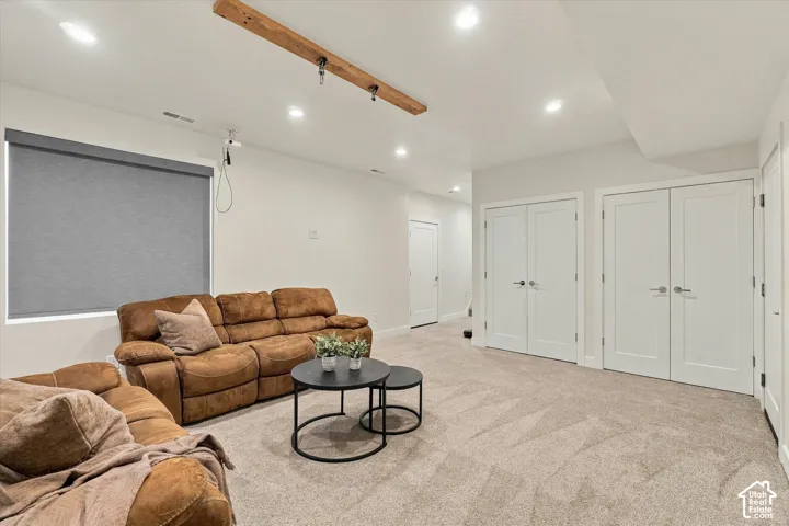 Recessed lighting throughout, light-toned carpeting, wood beam ceiling accent, white interior doors, and a window with a roller shade