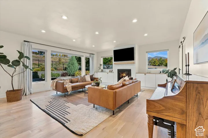 Spacious living area featuring light wood-finish flooring, a contemporary fireplace with a tiled surround, recessed lighting, and large windows