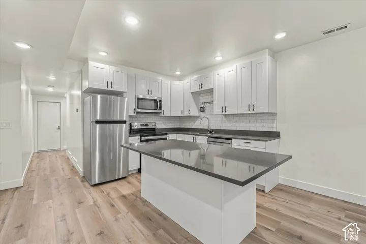 Modern kitchen featuring stainless steel appliances, white cabinetry, a central island with a solid surface countertop, wood-finish flooring, and recessed lighting
