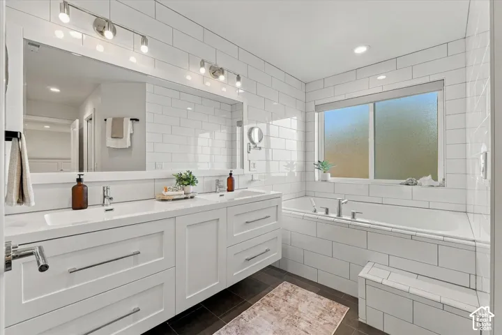 Dual vanity with integrated sinks, white shaker cabinetry, large format mirror, subway tile shower surround, and a built-in bathtub