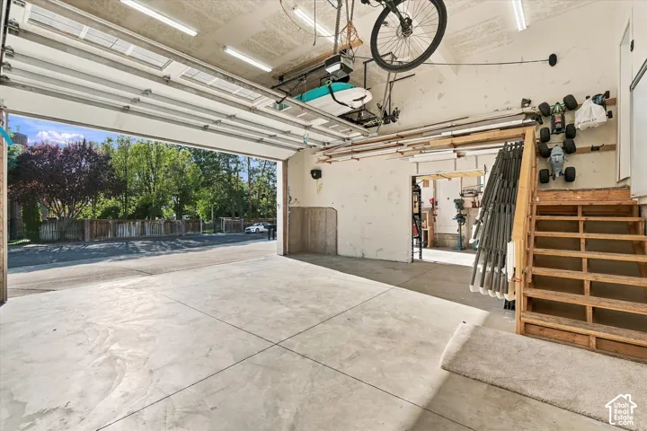 Concrete floor garage with an automatic overhead door, wood-finish stairs, and overhead fluorescent lighting