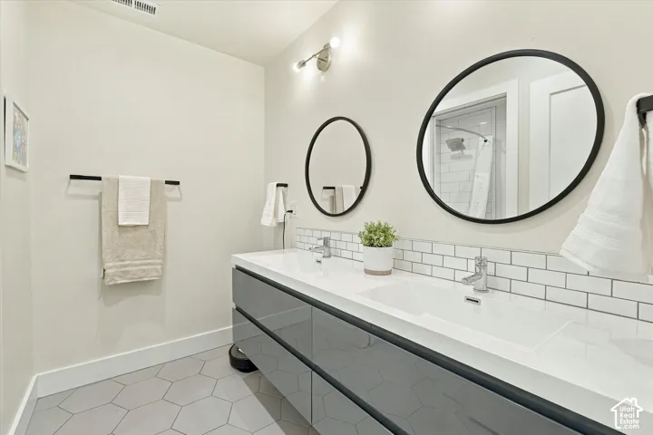 Dual rectangular undermount sinks set into a white countertop, subway tile backsplash, hexagonal floor tiles, and a double vanity with dark gray cabinetry