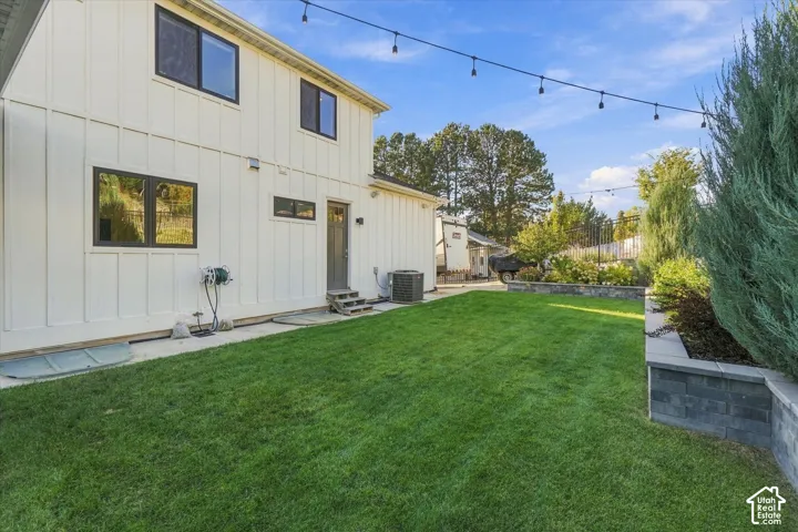 Manicured lawn with a stone retaining wall, board and batten siding, dark-framed windows, and string lights