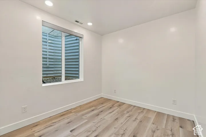 Recessed lighting, wood-finish flooring, white walls, and a window with a window well