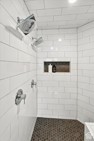 Spa-inspired shower featuring subway tile walls, dual showerheads with individual controls, a recessed niche with decorative tile accents, hexagonal floor tile, and integrated lighting throughout