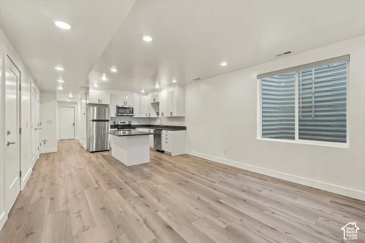 Open-concept living space with wood-finish flooring, recessed lighting, and a kitchen featuring white cabinetry, black countertops, and stainless steel appliances