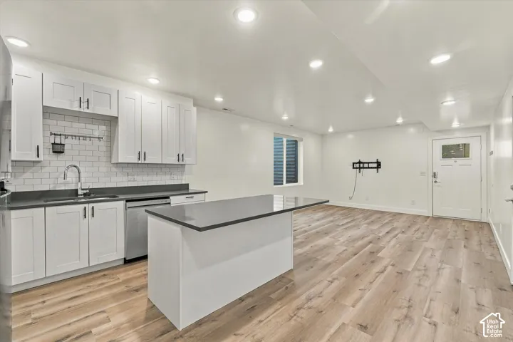 Open-concept living space with wood-finish flooring, recessed lighting, and a modern kitchen featuring white shaker cabinetry and a dark countertop island