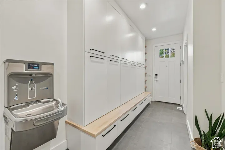 White shaker-style cabinetry with black hardware, integrated wooden bench, recessed lighting, and grey tile flooring
