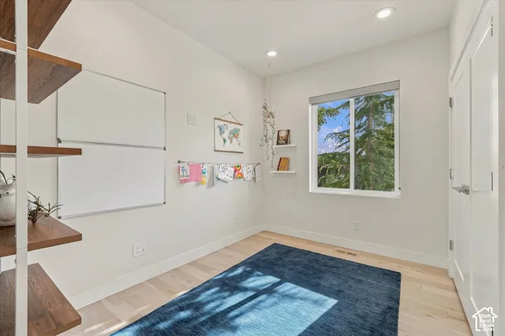 Recessed lighting, wood-finish flooring, white walls, built-in floating shelves, and a window with a roller shade