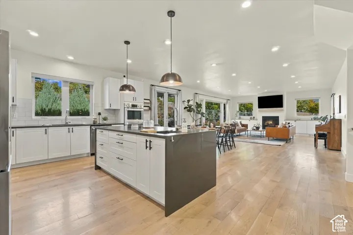 Open-concept living space featuring wood-finish flooring, a kitchen island with pendant lighting, white cabinetry, and a fireplace
