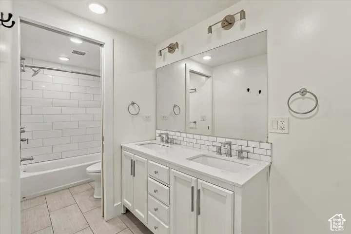 Double vanity with white cabinetry and integrated sinks, subway tile backsplash, and a shower-over-tub combination with subway tile surround