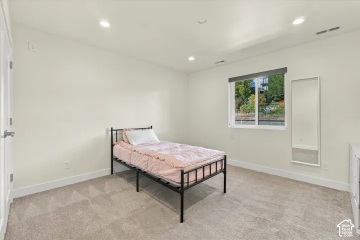 Recessed ceiling lighting, white interior door, light neutral-toned walls, double-pane window with roller shade, and plush carpet flooring