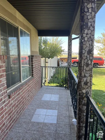 Covered patio with a tiled floor, decorative wrought iron railing, and a stone-clad support column