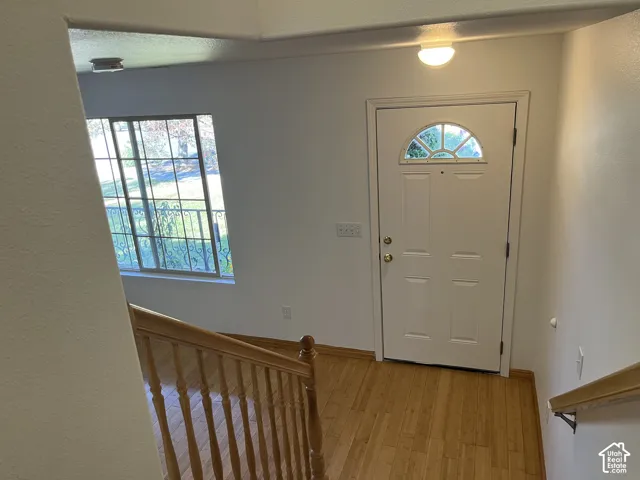 Entryway featuring wood-finish flooring, a white paneled door with an arched window, and a wood railing