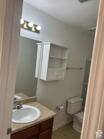 Vanity with an integrated sink and laminate countertop, wood-finish cabinetry, wall-mounted light fixture, white wall-mounted storage cabinet, and tile flooring