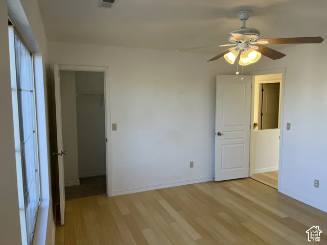 Wood-finish flooring, ceiling fan with integrated lighting, white paneled doors, and a window with natural light