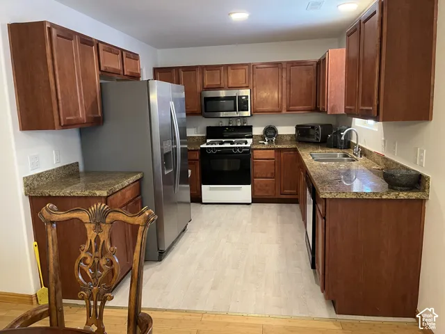 Kitchen featuring wood-finish cabinetry, stone countertops, stainless steel appliances, and light wood-look flooring