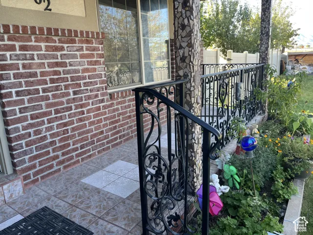 Brick siding detail, decorative wrought iron railing, tiled porch floor, and established landscaping