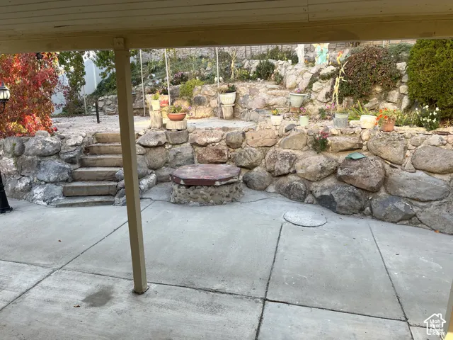 Paved concrete patio area featuring a stone retaining wall, natural stone steps, and a circular stone-built feature