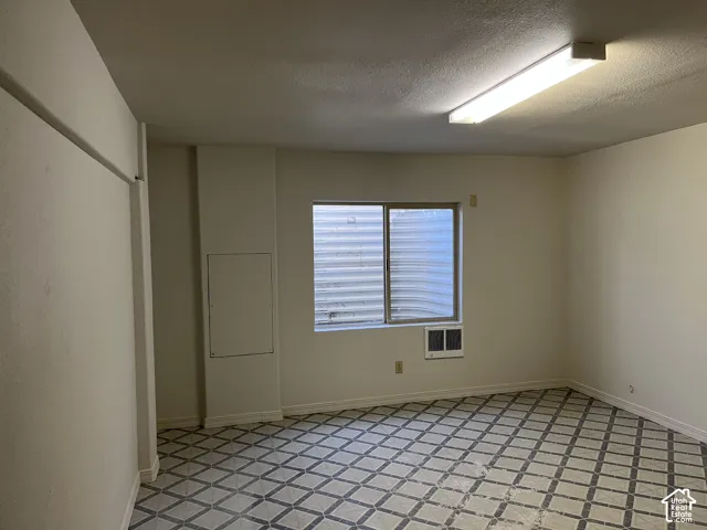 Recessed window featuring a security grate, floor-mounted air conditioning unit, fluorescent overhead lighting, and patterned flooring