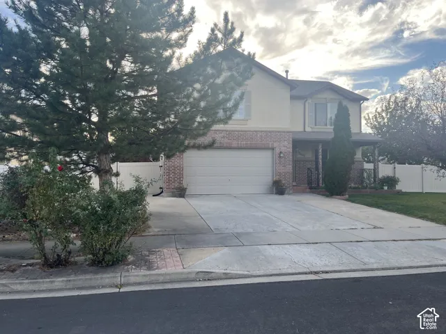Two-story stucco and brick exterior, attached garage, covered porch entry, mature landscaping, and concrete driveway