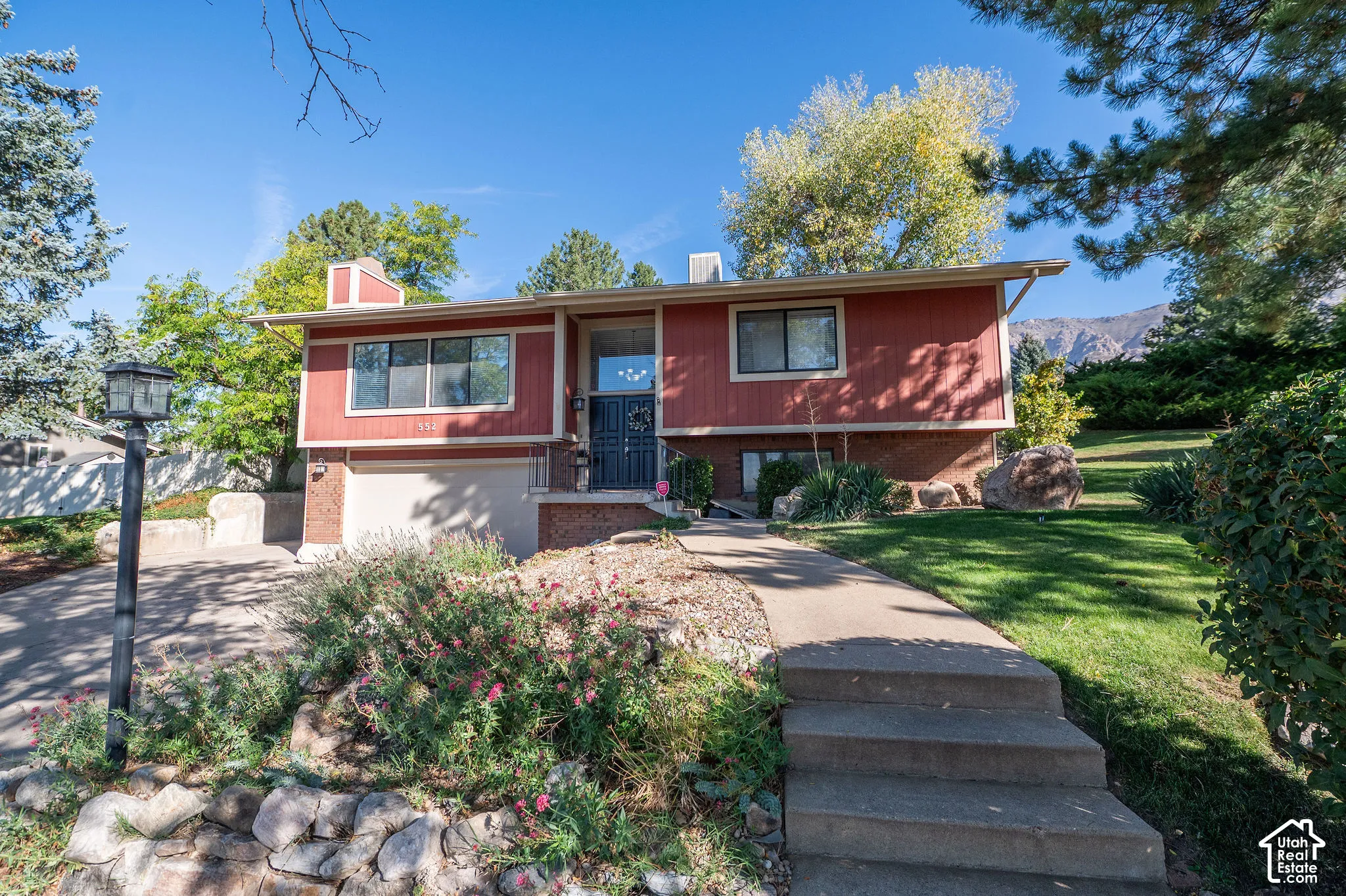Red-sided exterior with brick accents, attached garage, concrete driveway, and a front walkway with steps