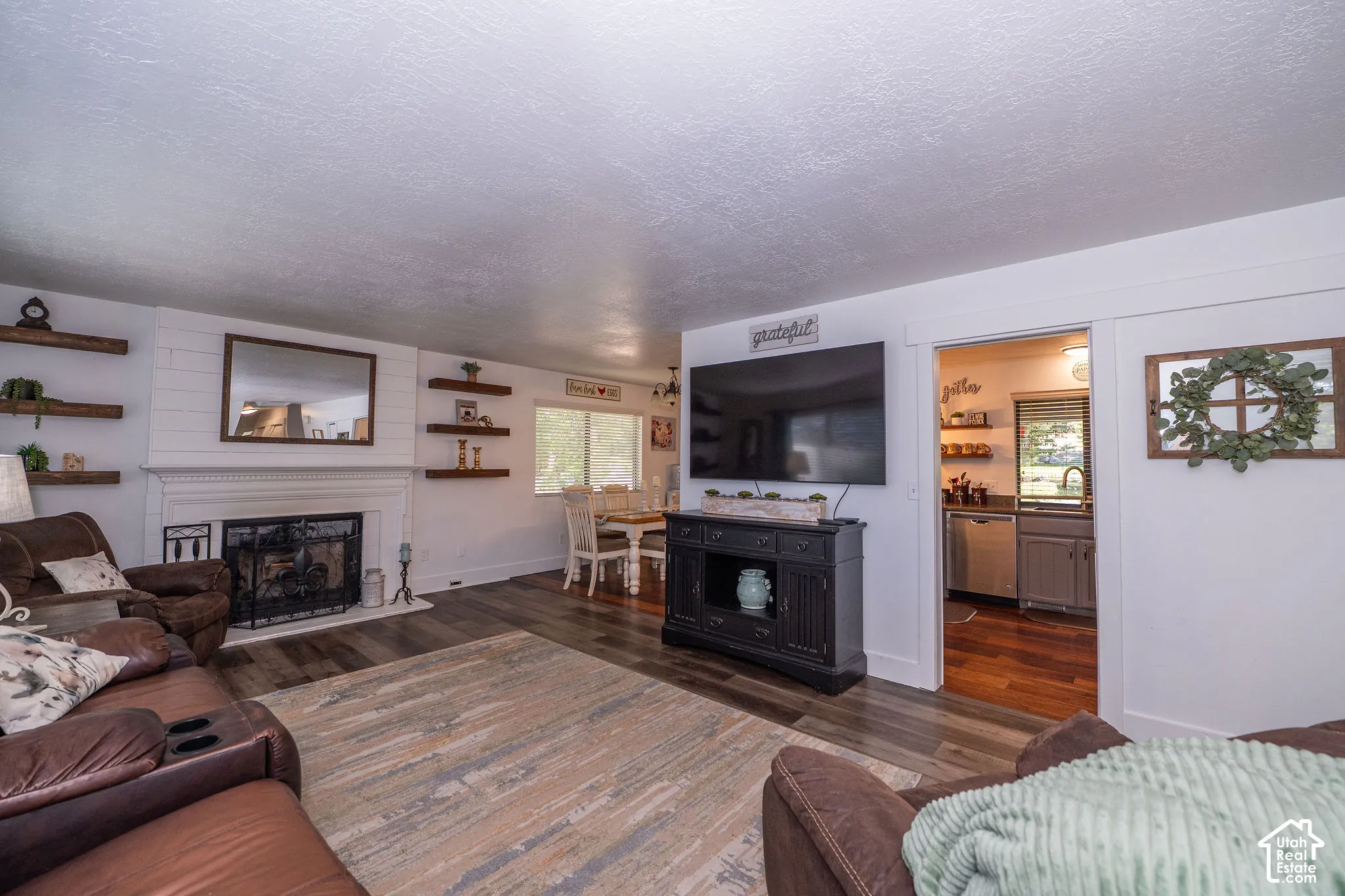 Living area with wood-finish flooring, a white mantel, and a fireplace with an iron grate