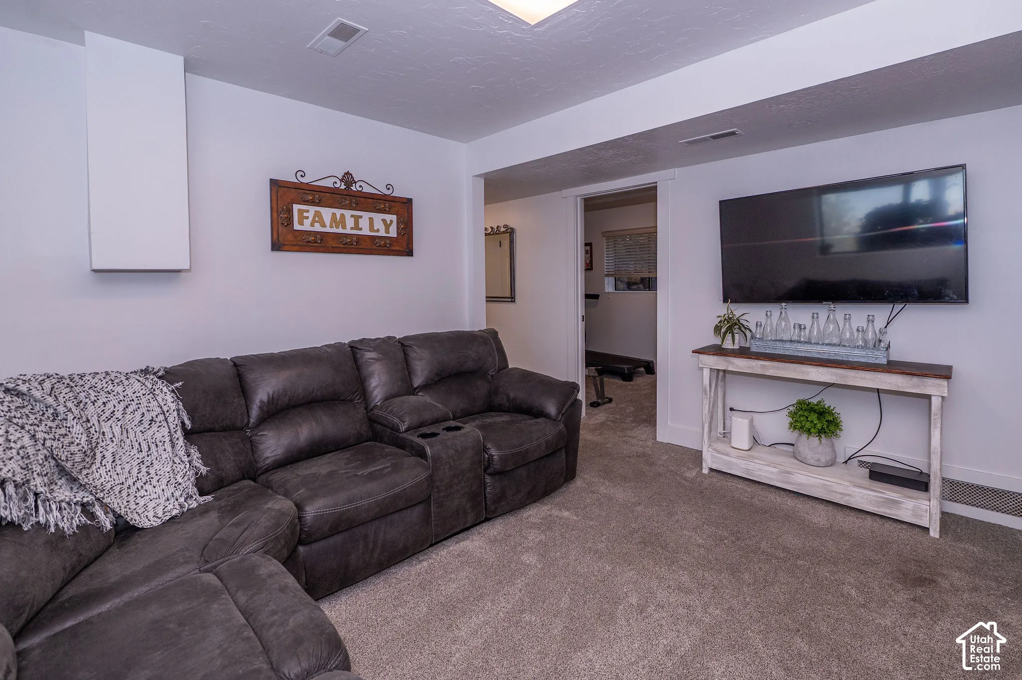 Carpeted flooring throughout, recessed ceiling lighting, light-toned wall finishes, and a wall-mounted television