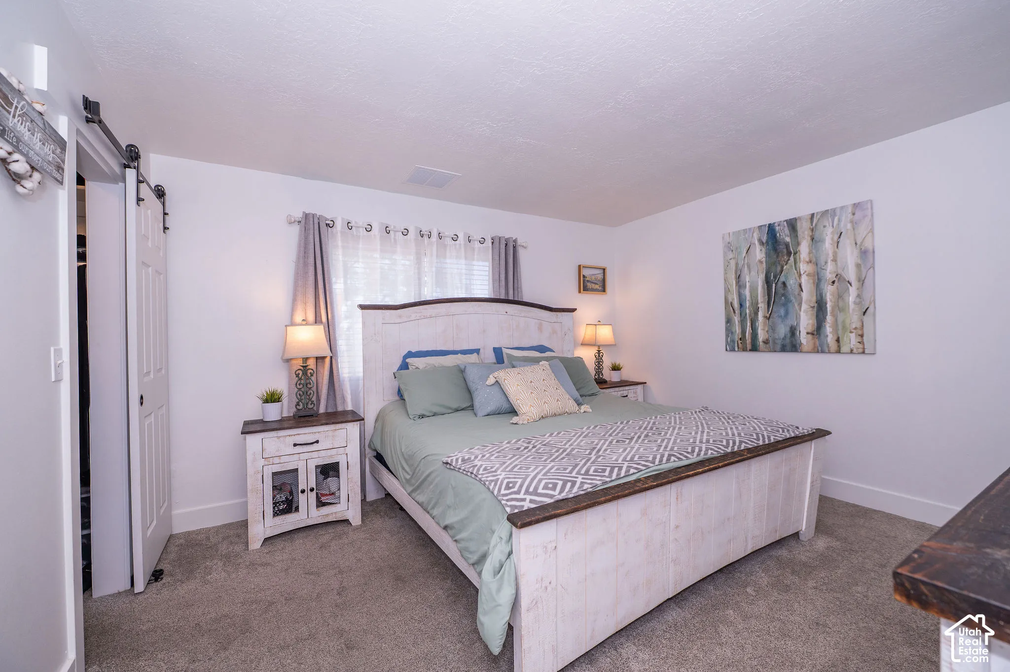 Primary bedroom with white walls, gray carpet, and a white barn door