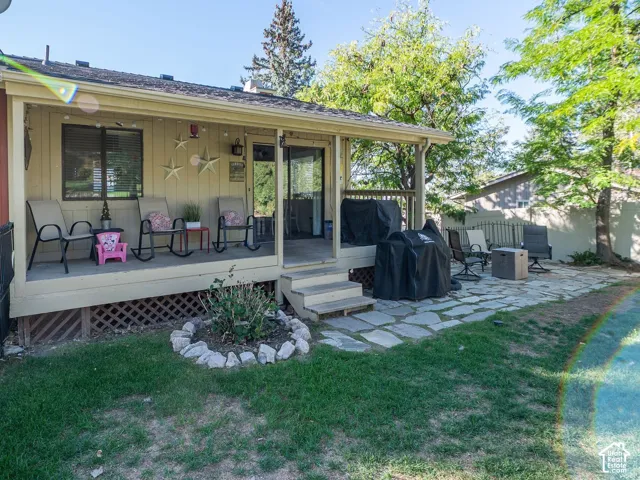Backyard Covered porch with wood-finish decking, stone patio, manicured lawn, and privacy fencing