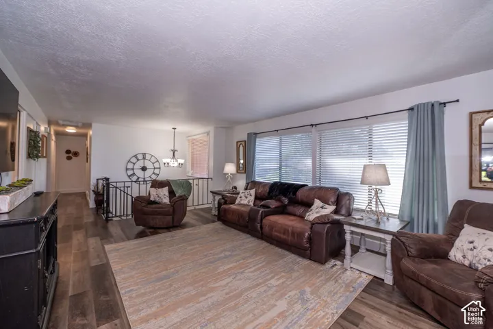 Spacious living area featuring wood-finish flooring, multiple windows with blinds, and a prominent chandelier