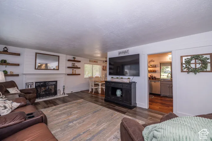 Living area with wood-finish flooring, a white mantel, and a fireplace with an iron grate