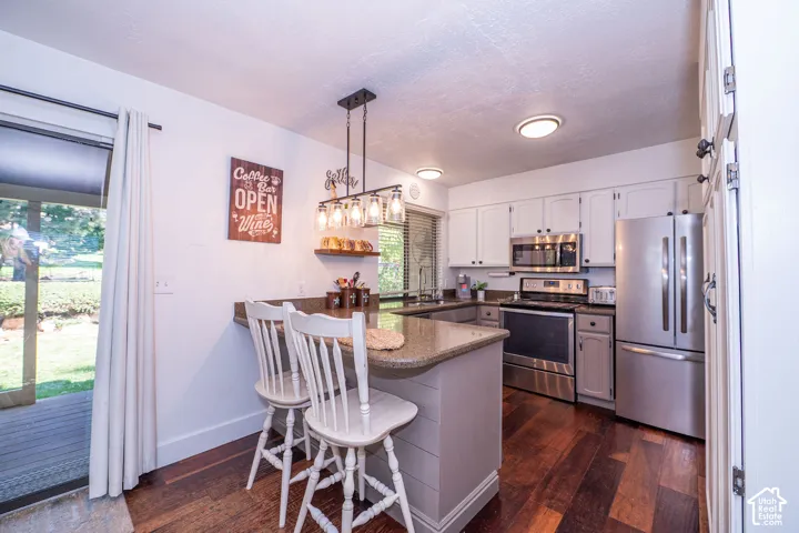 Kitchen featuring stainless steel appliances, wood-finish flooring, white cabinetry, a built-in breakfast bar, and a sliding glass door