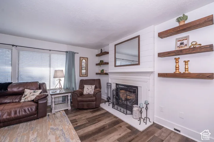 Fireplace with a white mantel, wood-finish flooring, white shiplap accent wall, and floating wood shelves