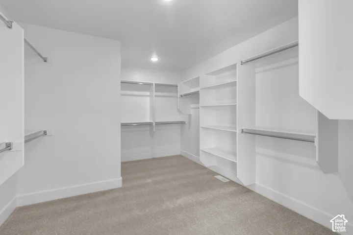 Spacious closet with built-in shelving, chrome hanging rods, recessed lighting, and light-colored carpet