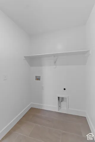 Laundry utility space featuring a wall-mounted shelf, light-toned tile flooring, and utility hookups