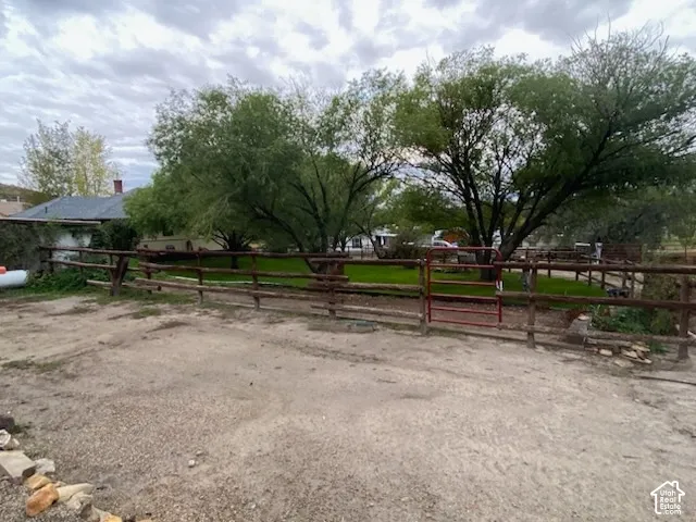 Gravel lot with wood fencing and a red metal gate, bordering a grassy area with mature trees