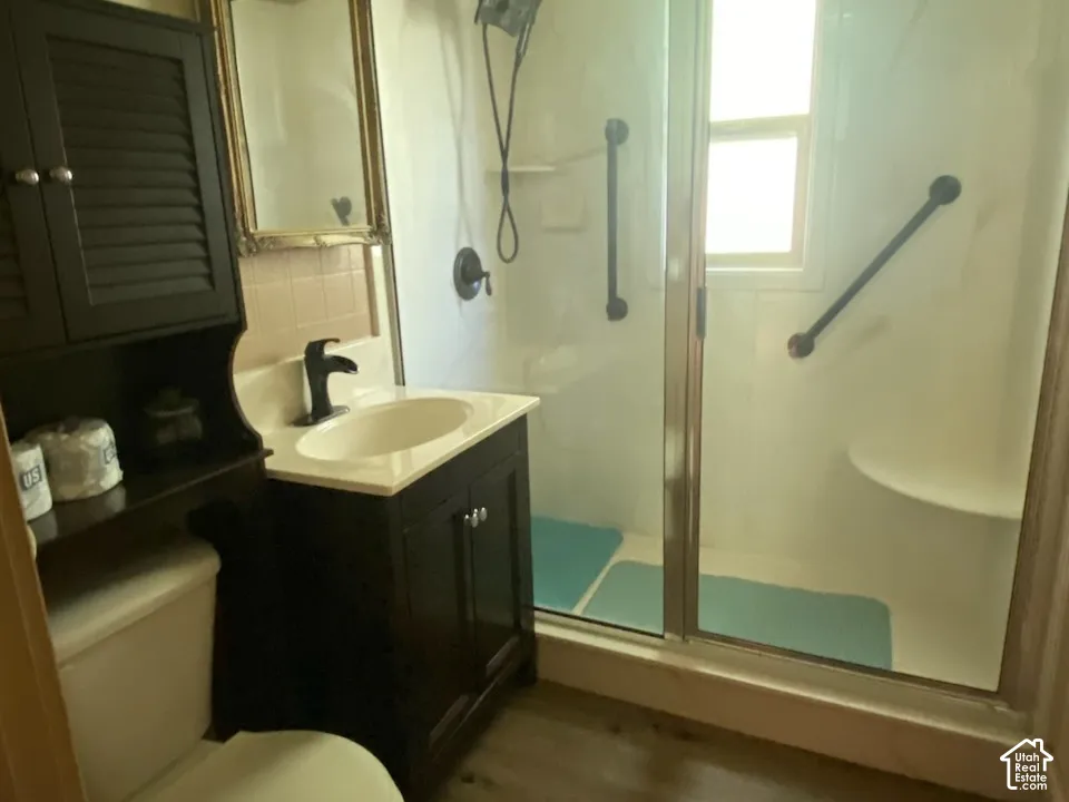 3/4 bathroom located by both bedrooms. Walk-in shower with sliding glass doors, built-in shower bench, dark wood-finish vanity with countertop sink, and wood-finish flooring