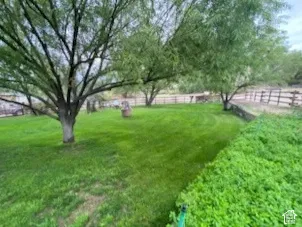 Expansive green lawn with mature trees, bordered by a low stone wall and a wooden fence